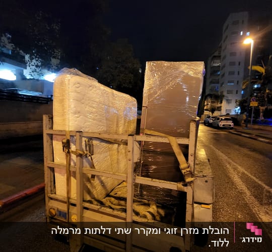 מזרנים וארגזים על עגלה ברחוב בלילה